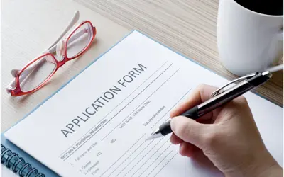 A hand filling out an application form with eye glasses and a coffee cup besides